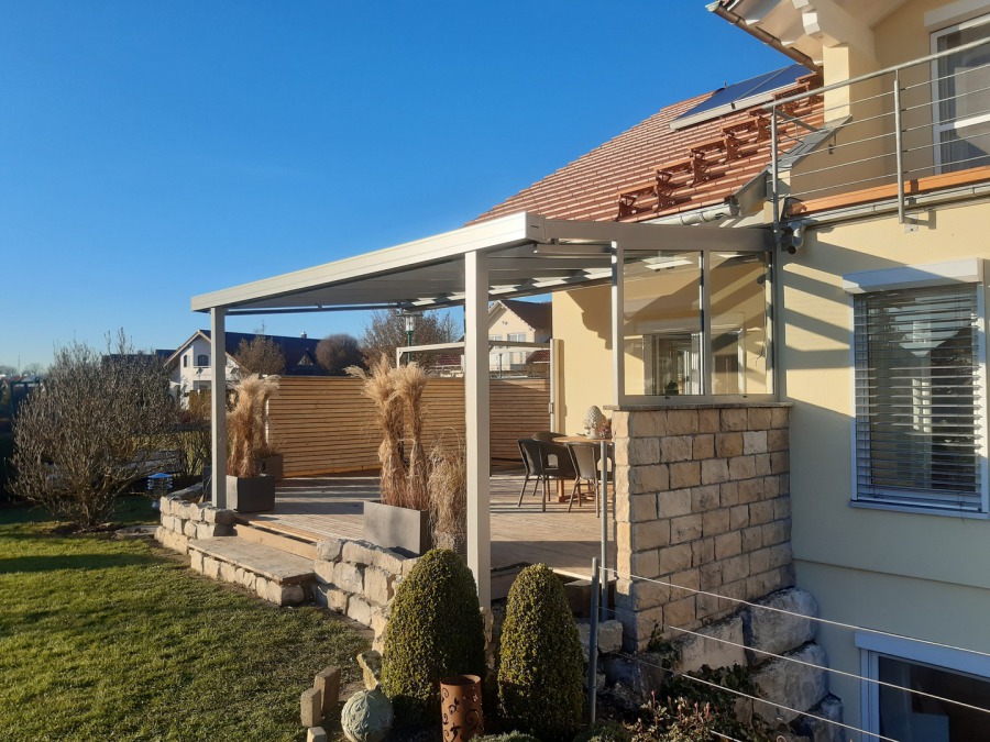 Dunkle Terrassenüberdachung mit seitlicher Verglasung am Wohnhaus.