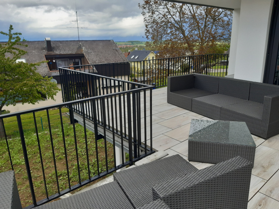 Dunkles Stabgeländer entlang einer Terrasse mit Sitzbereich.